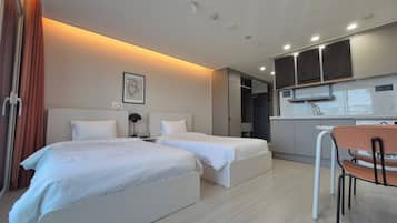A hotel room with two beds, a small kitchenette, and a dining area.
