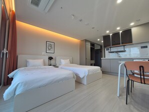 Habitación de hotel con dos camas, una kitchenette pequeña y una zona de comedor.