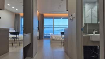Habitación de hotel con cama, escritorio, silla, baño con lavamanos y espejo, y ventana grande con vistas.