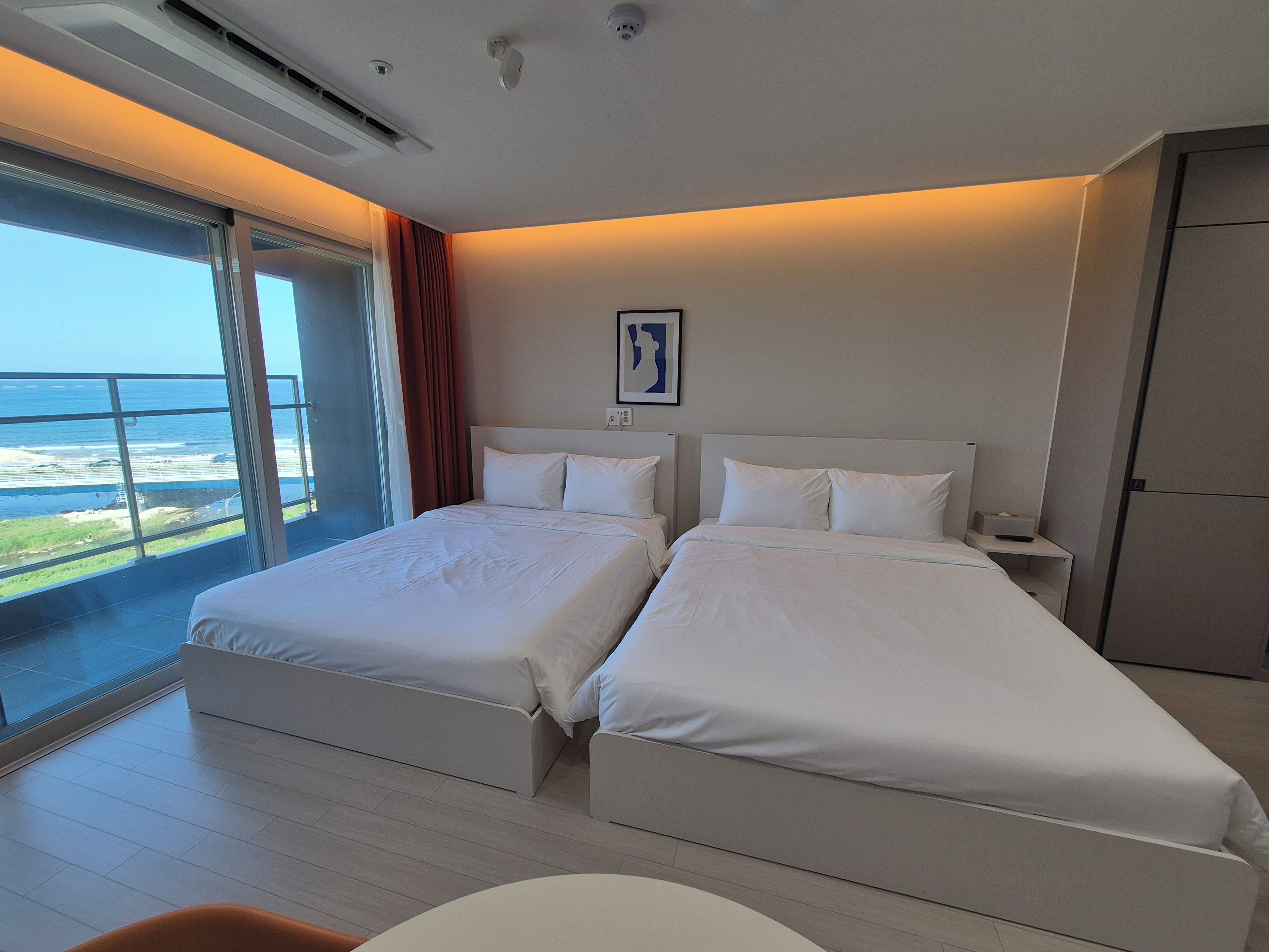 A hotel room with two beds, a large window with a view of the beach, and a small table.