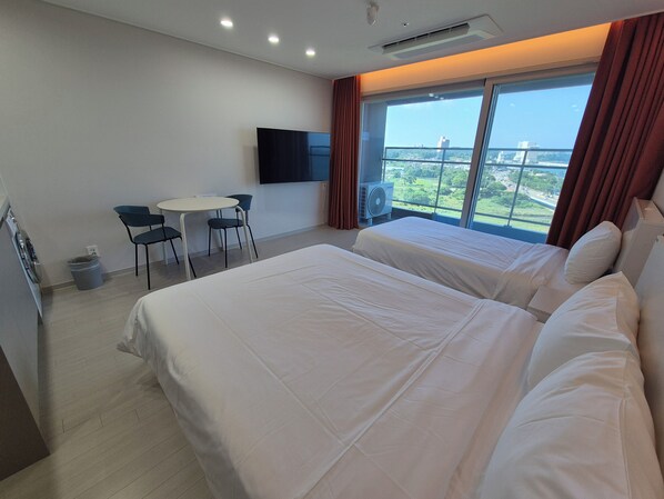 Habitación de hotel con una cama grande, un escritorio, dos sillas, un televisor y una ventana con vistas a la ciudad.