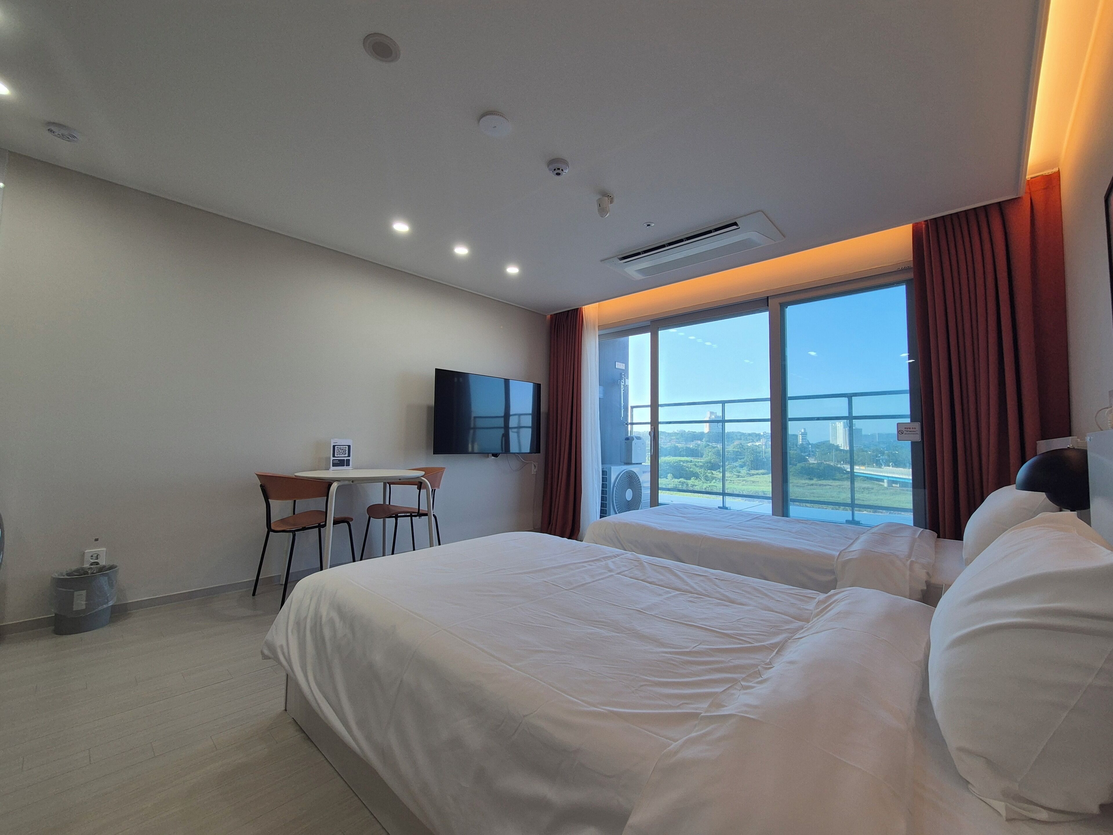 A hotel room with a large bed, a desk with a chair, a flat-screen TV, and a large window with a view.