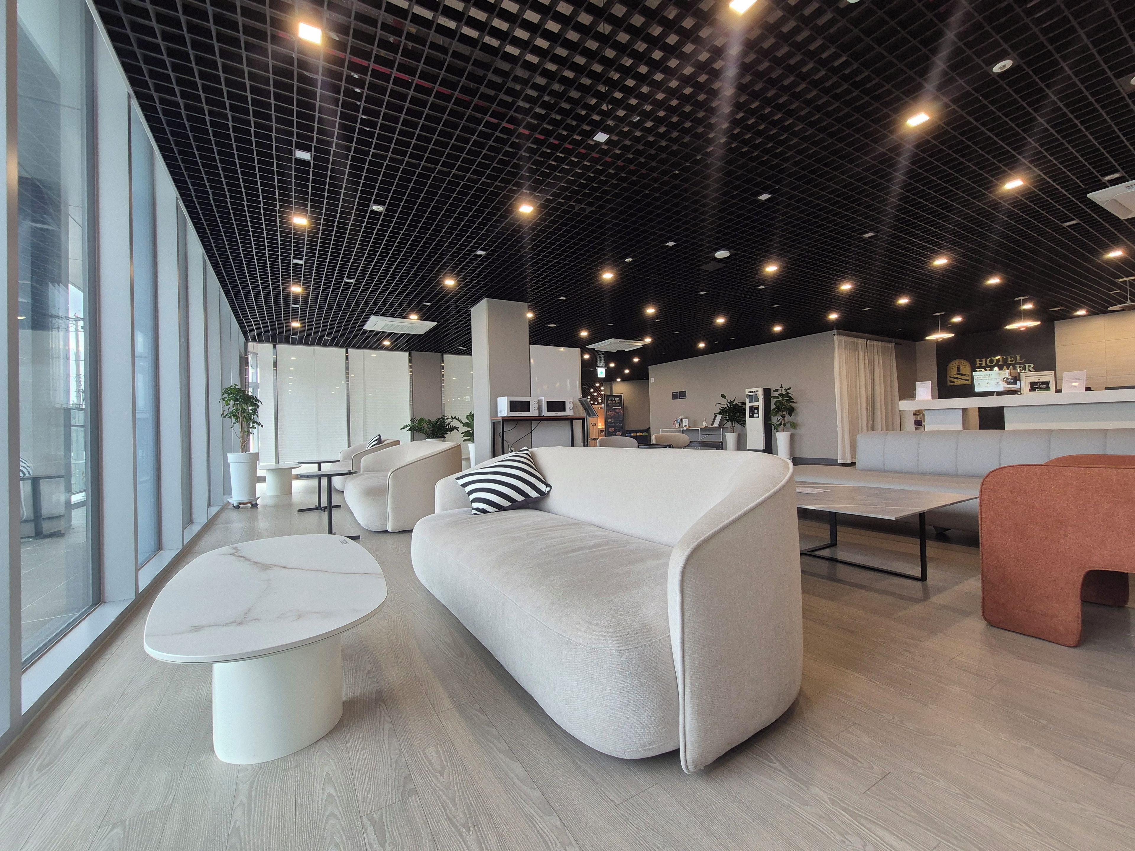 A modern hotel lobby with seating areas, a reception desk, and a large window providing natural light.