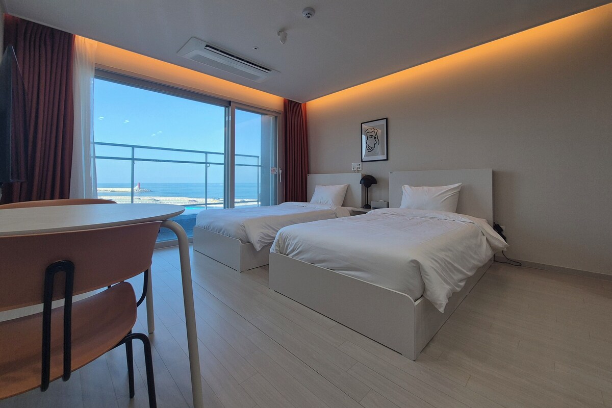 A hotel room with two beds, a desk, and a view of the ocean.