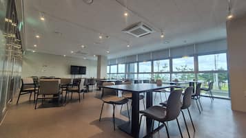 Un salón de conferencias amplio con una gran mesa y sillas, un televisor de pantalla plana en la pared y ventanas grandes con vistas al exterior.