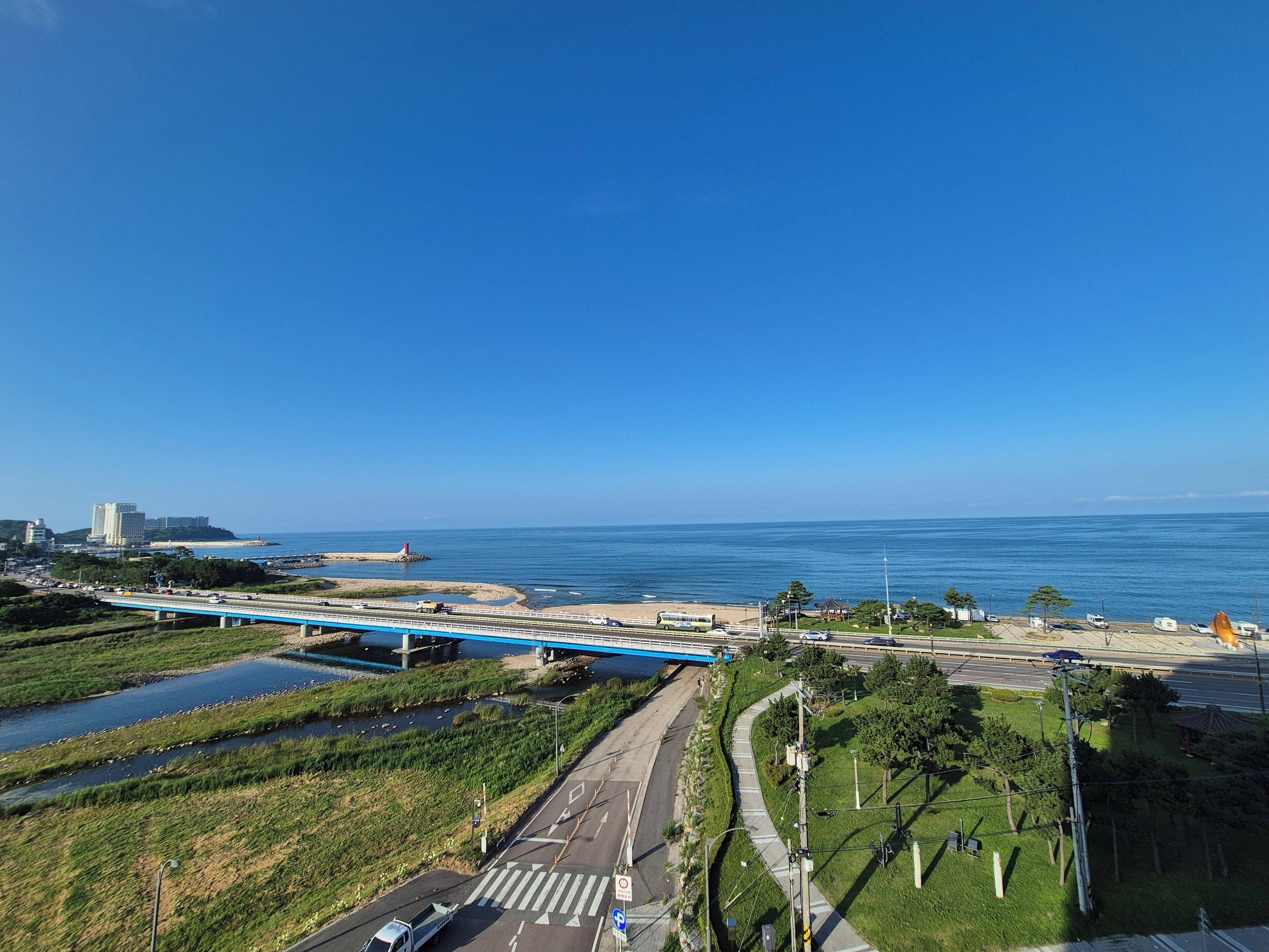 A coastal road with a blue bridge, a beach, and a lighthouse.