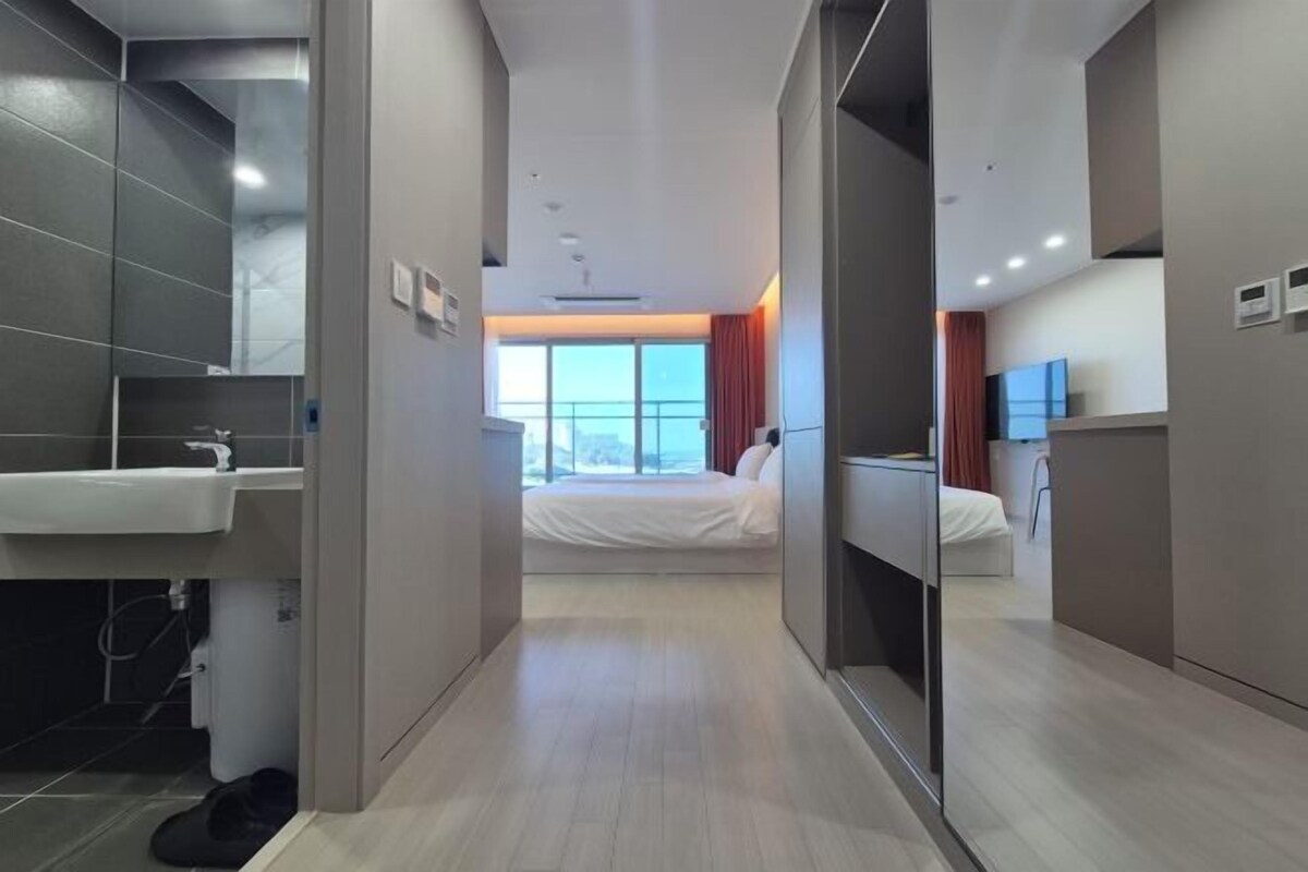 A modern hotel room with a bed, a bathroom with a sink, and a large window providing a view.
