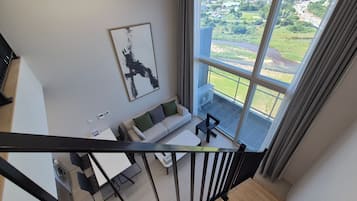A modern living room with a sofa, a coffee table, and a view of a green landscape through large windows.