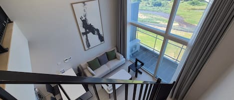 A modern living room with a sofa, a coffee table, and a view of a green landscape through large windows.