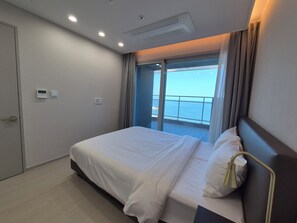 Una habitación de hotel con cama, ventana con cortinas, puerta y una lámpara en el techo.