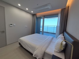 Una habitación de hotel con cama, ventana con cortinas, puerta y una lámpara en el techo.