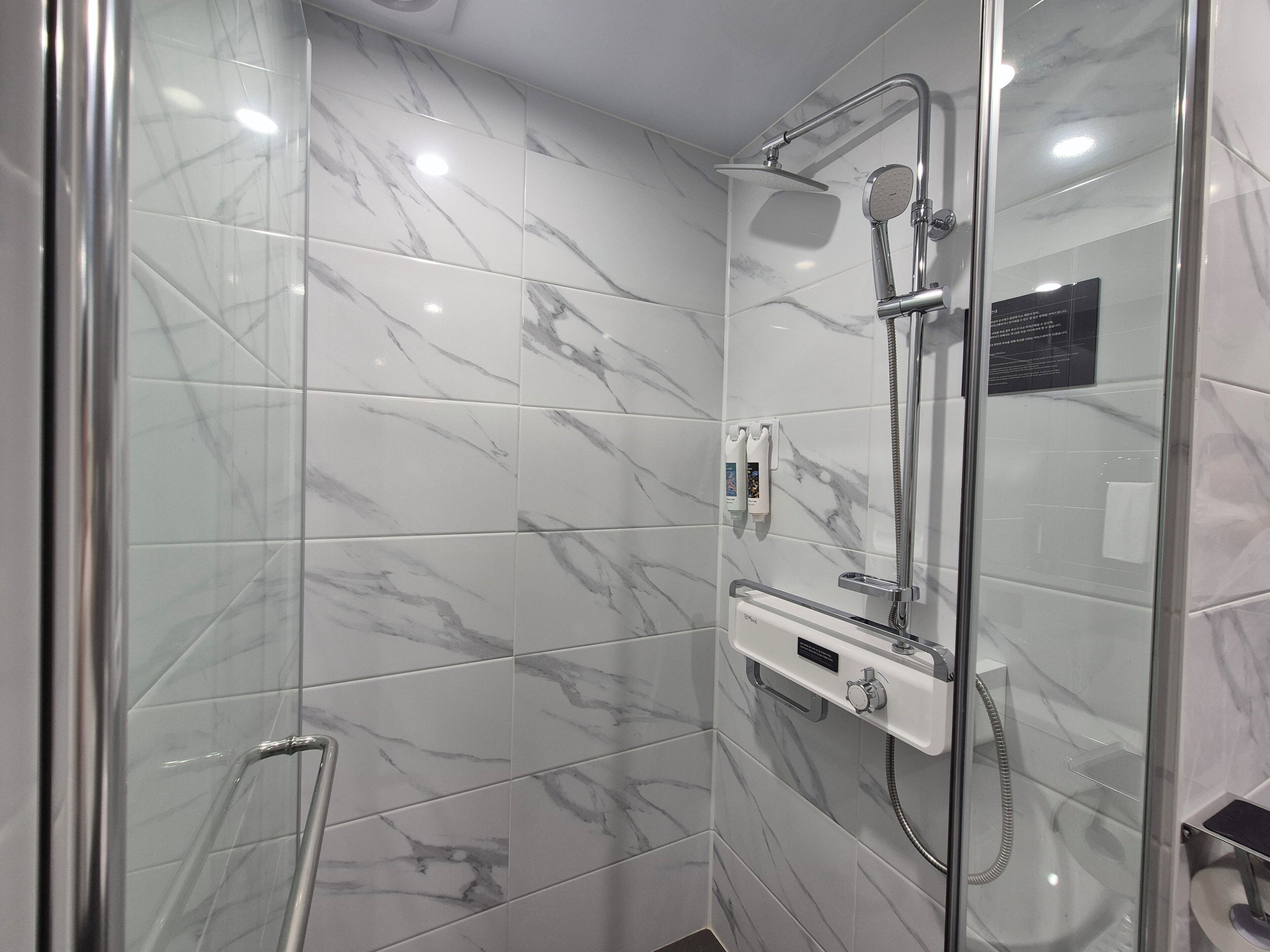 A modern bathroom with a glass-enclosed shower, marble tiles, and a handheld showerhead.