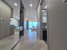 Un corredor moderno de hotel con suelo de madera, una zona de estar con sillas, un escritorio y un amplio ventanal con vistas.