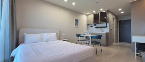 A hotel room with a large bed, a small kitchenette, and a bathroom.