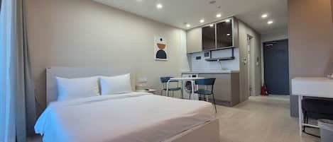 A hotel room with a bed, a small kitchenette, a bathroom, and a shower area.