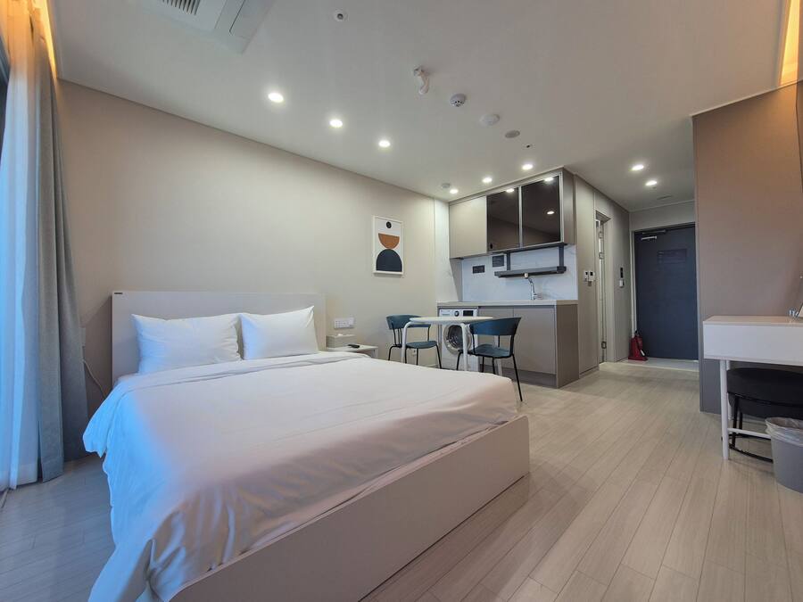 A hotel room with a bed, a small kitchenette, a bathroom, and a shower area.