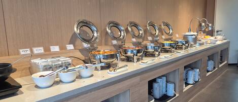 A buffet setup with multiple serving stations, each with a lid and labeled with a name.