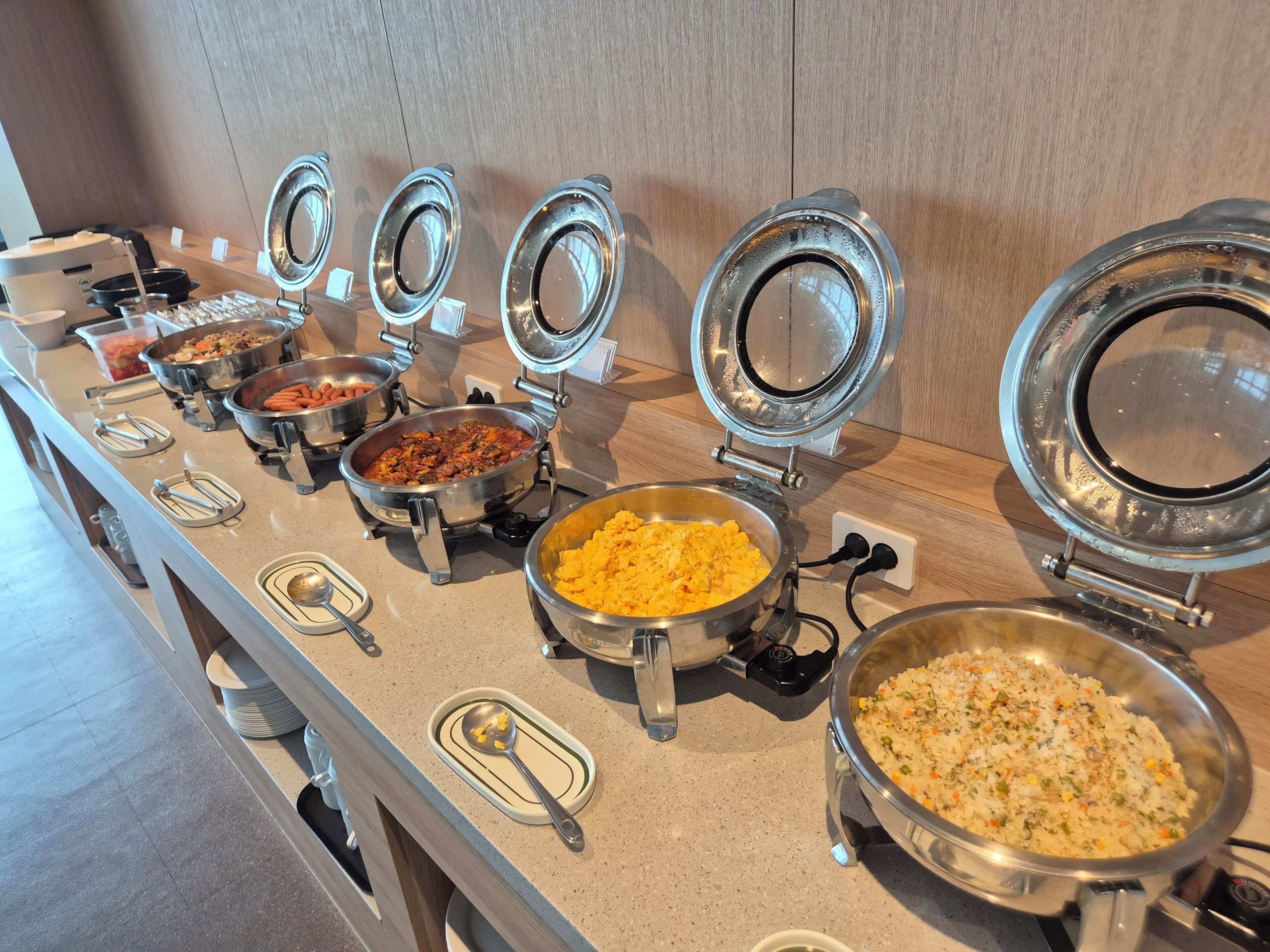A buffet line with various dishes in metal serving containers, some with lids open.