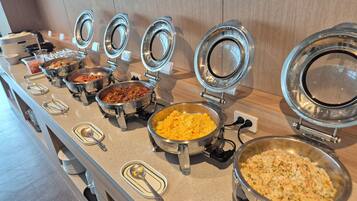A buffet line with various dishes in metal serving containers, some with lids open.