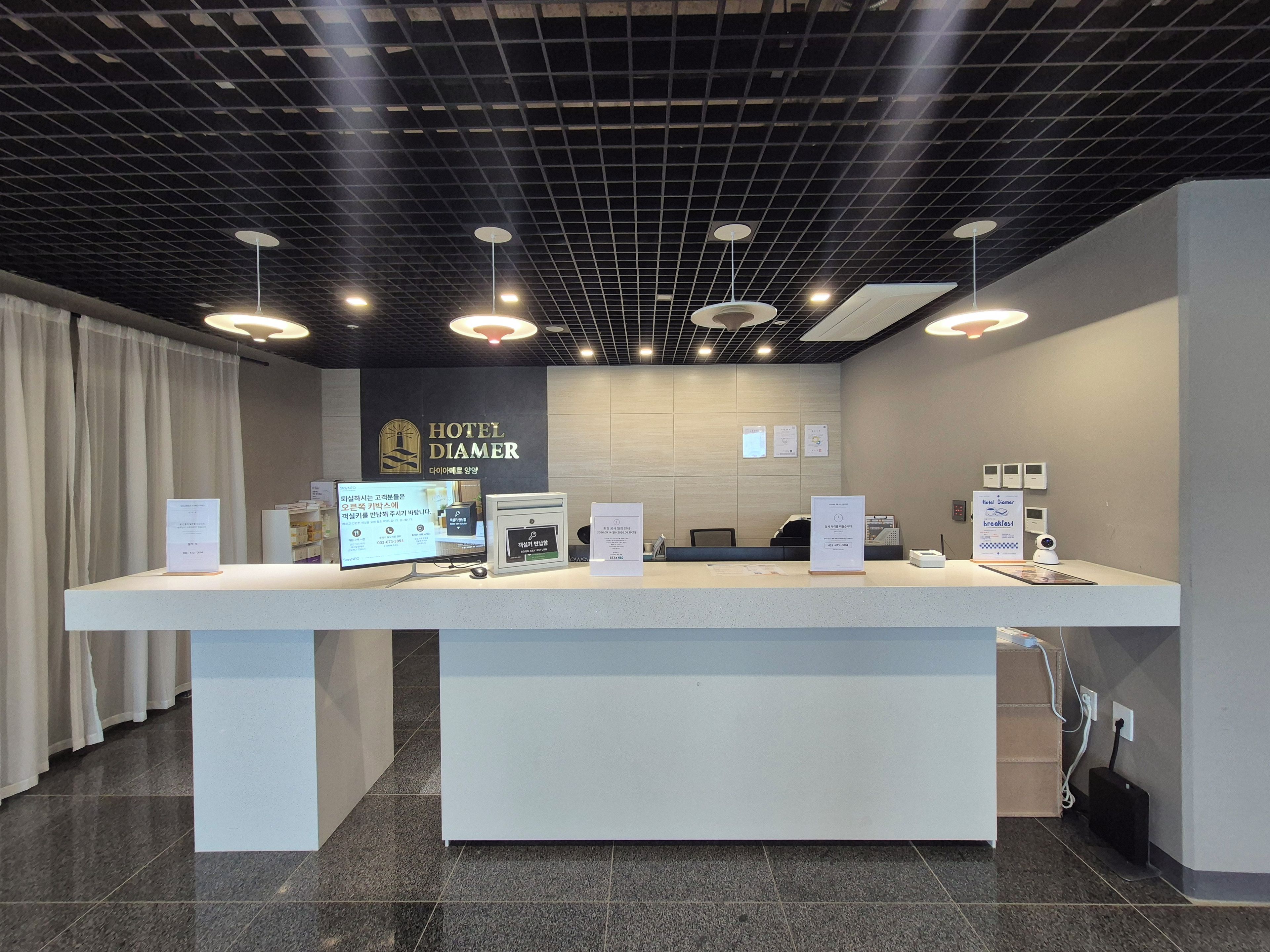 Un mostrador de recepción de hotel con diseño moderno, que incluye una pantalla digital, una computadora y un cartel.