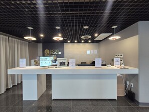 A hotel reception desk with a modern design, including a digital display, a computer, and a signboard.