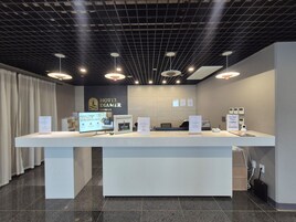 Un mostrador de recepción de hotel con diseño moderno, que incluye una pantalla digital, una computadora y un cartel.