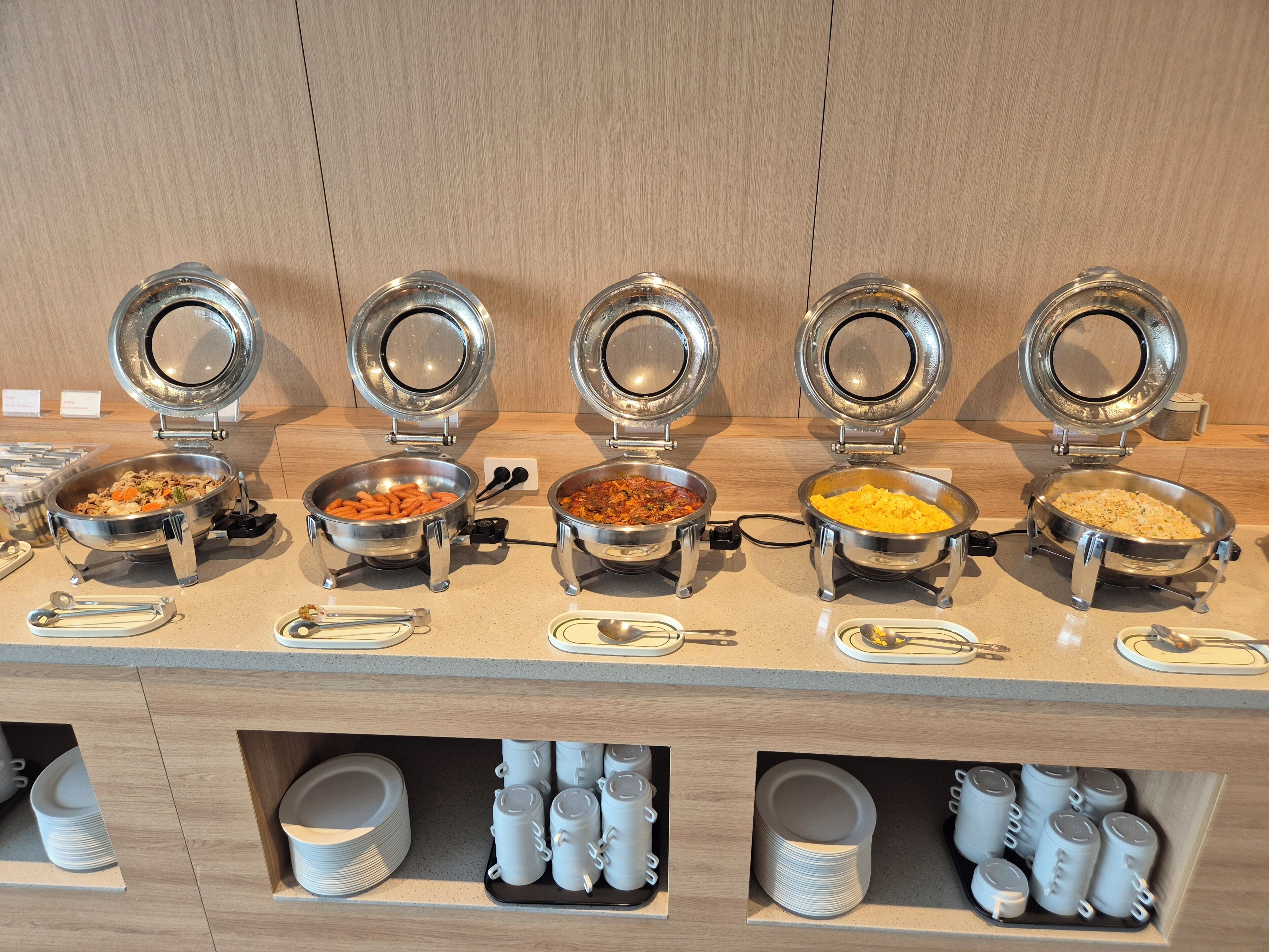 A buffet setup with multiple food stations, each with a metal bowl and a lid.