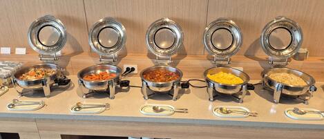 A buffet setup with multiple food stations, each with a metal bowl and a lid.