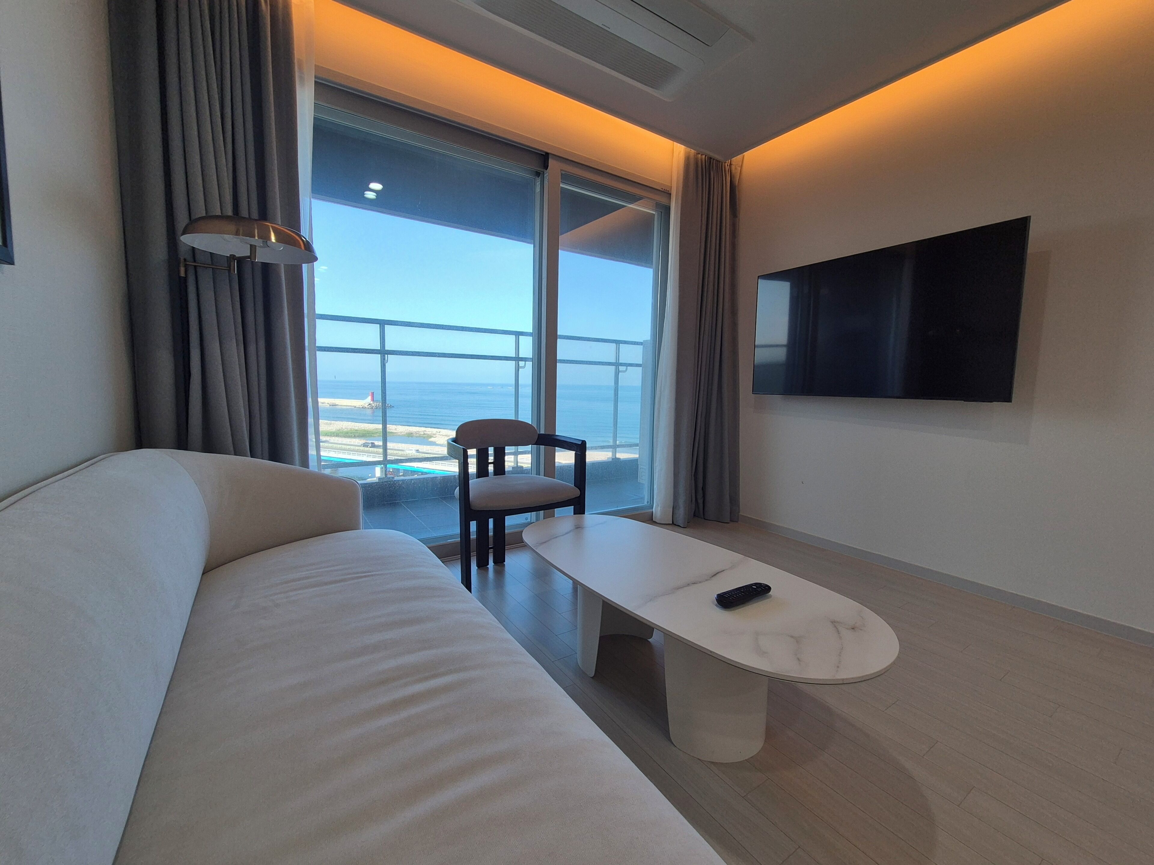 Habitación de hotel moderna con sofá, una mesita, una silla, un televisor y vistas al mar.