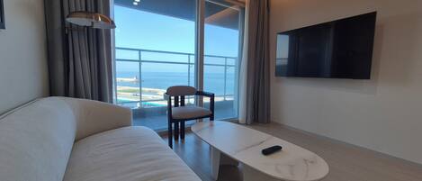 Habitación de hotel moderna con sofá, una mesita, una silla, un televisor y vistas al mar.