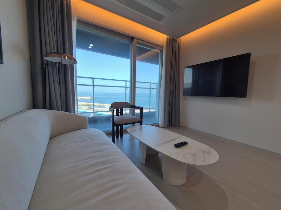 Habitación de hotel moderna con sofá, una mesita, una silla, un televisor y vistas al mar.
