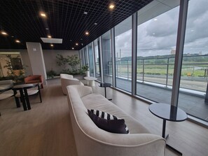 A modern lounge area with a sofa, chairs, and a small table, featuring large windows with a view of a road and greenery. - Diamer Hotel Yangyang By Stayneo (Yangyang)