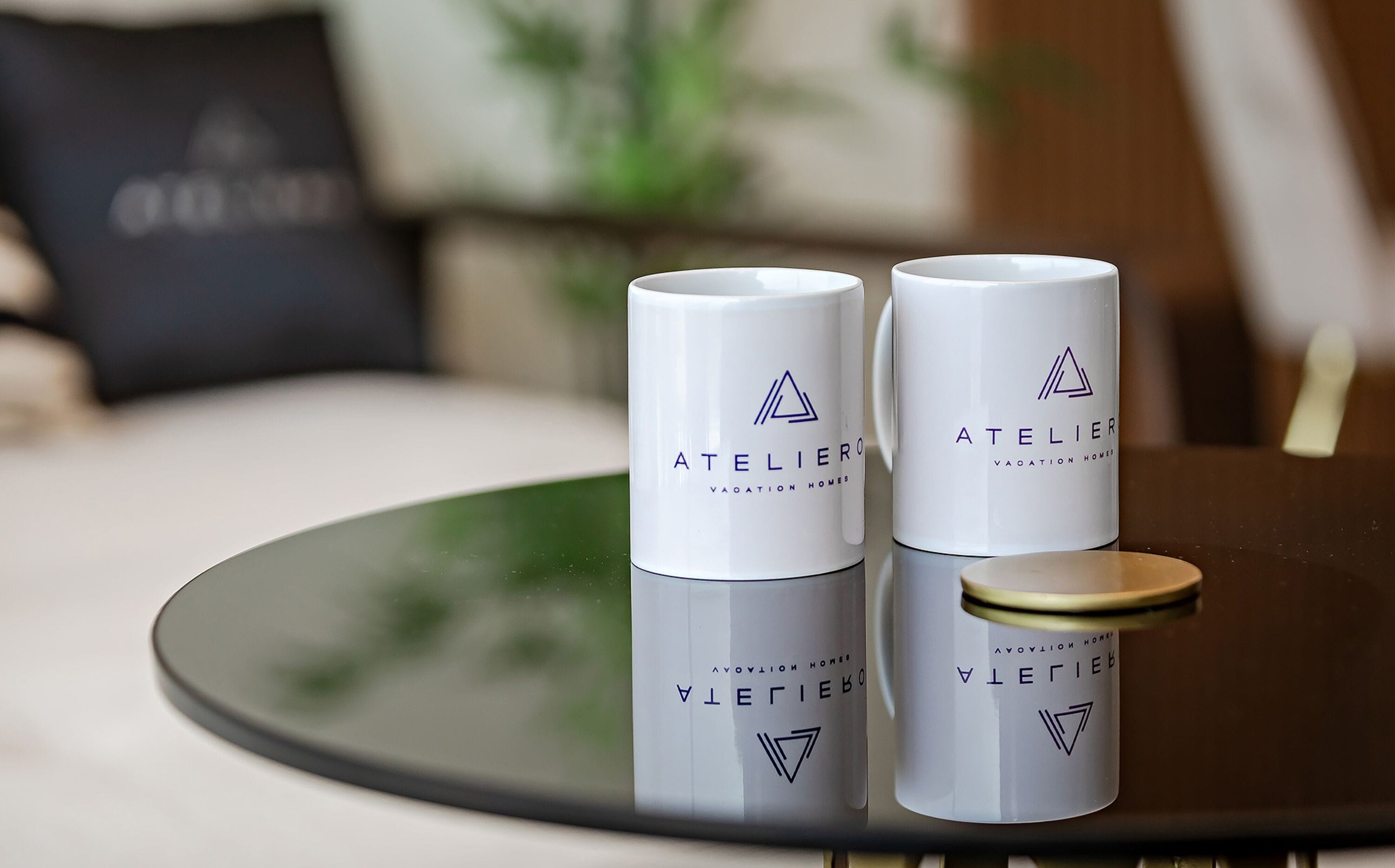 Deux récipients cylindriques blancs, portant l’étiquette « ATELIER », sont posés sur une table en verre réfléchissant.