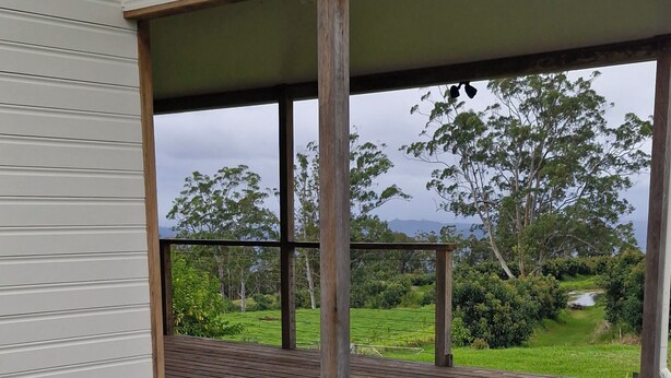 A wooden deck with steps leading to a covered porch, overlooking a lush green landscape with trees and a view of the sky.