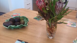 A modern kitchen with white cabinets, a coffee machine, and a sink. There is a bowl of fruit on the table and a vase with flowers.