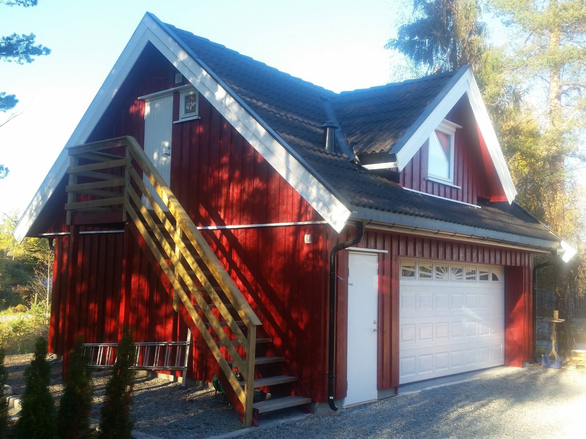 Une grange rouge avec une porte de garage blanche, un escalier en bois et un toit en métal.