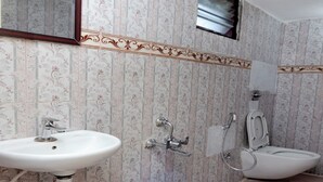 A bathroom with a sink, toilet, shower, and a blue bucket on the floor. - ASK Grande Residency (Puducherry)