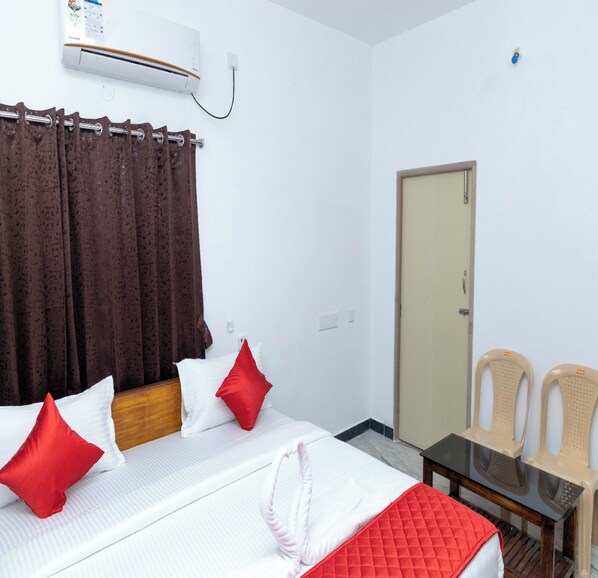 A hotel room with a bed, a table, two chairs, a door, and an air conditioning unit. - ASK Grande Residency (Puducherry)