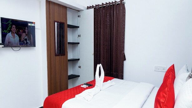 A neatly made bed with a red and white bedspread, a wooden headboard, and a television mounted on the wall. - ASK Grande Residency (Puducherry)