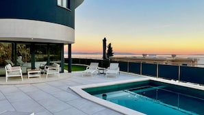 Un espace piscine extérieur moderne, doté de chaises longues et offrant une vue sur le coucher de soleil sur l’eau.