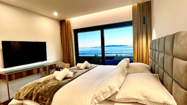 Une chambre d’hôtel avec un grand lit, un téléviseur à écran plat, une vue sur la mer et une fenêtre avec des rideaux.