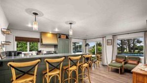 Une cuisine moderne dotée d’un îlot central, de tabourets de bar et d’un coin repas offrant une vue sur l’extérieur.