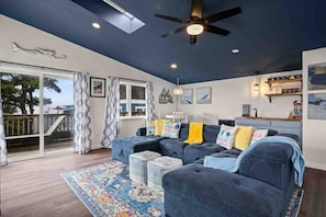 A modern living room with a dark ceiling, a ceiling fan, and a large window with curtains.