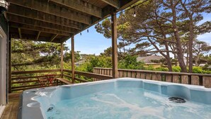 Un bain à remous situé sous une terrasse en bois, avec vue sur les arbres et une maison en arrière-plan.
