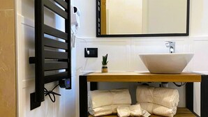 Une salle de bain équipée d’un porte-serviettes, d’un lavabo avec un miroir et d’une étagère avec des serviettes.