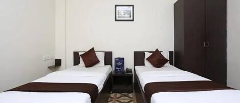 A hotel room with two single beds, a wardrobe, a framed picture on the wall, and a small table with a phone and a sign.