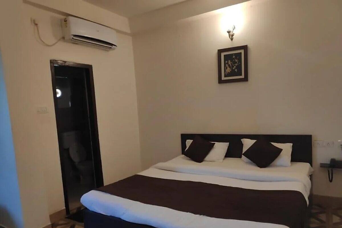 A hotel room with a bed, a door, an air conditioning unit, and a wall-mounted light fixture.