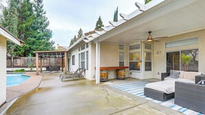 Uma área de varanda coberta com móveis de exterior, piscina e um pergolado.