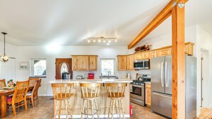 A modern kitchen with wooden cabinets, a central island with bar stools, stainless steel appliances, and a dining area with wooden chairs and a table. - Panoramic Mtn Views: 5-Acre Escape in Palmer! (Palmer)