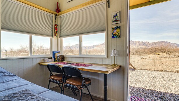 Ein Zimmer mit einem Bett, einem Schreibtisch mit zwei Stühlen, einem Fenster mit Jalousien und Blick auf die Berge.